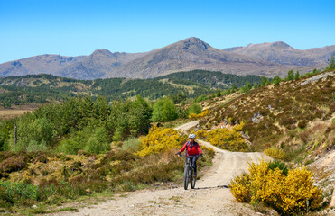 Obraz premium nice senior woman riding her electric mountain bike in the highlands of Glen Affric Nature reserve, Scotland, UK