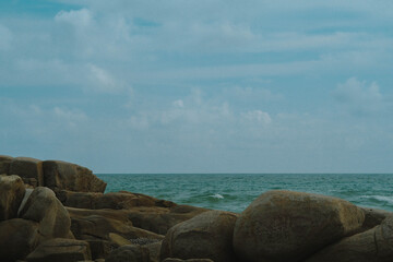 A rocky coastline meeting the blue sea under a cloudy sky.