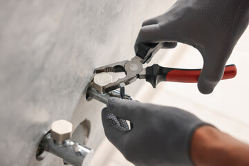 Man fixing water valve with pliers indoors, closeup