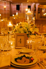 Elegant event table setup with candlelit centerpieces and floral arrangements in a banquet hall during evening hours