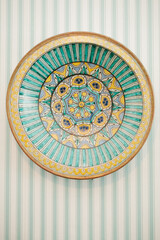 Colorful ceramic plate displayed on a striped wall in an artistic setting showcasing vibrant design and intricate details