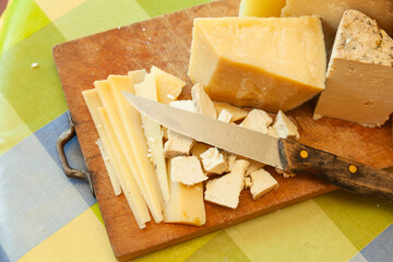 Close-up of sliced and crumbled hard cheeses with kitchen knife on rustic wooden board