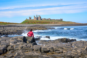 woman admiring medieval ruin of Dunstanburgh castle in north eastern England, UK