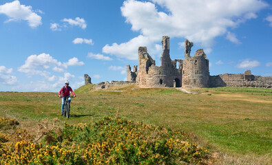 nice senior woman cycling with her elctric mountain bike at Dunstanburgh castle in north eastern...