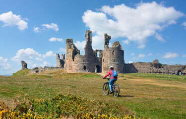 nice senior woman cycling with her elctric mountain bike at Dunstanburgh castle in north eastern England, UK