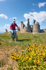 nice senior woman cycling with her elctric mountain bike at Dunstanburgh castle in north eastern England, UK