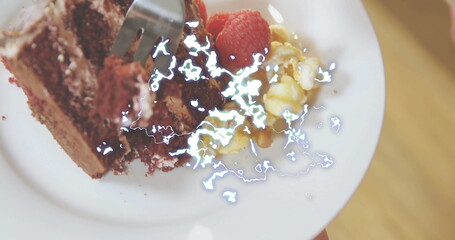 Holding white plate with chocolate cake slice over cafe table, showing raspberries, popcorn, fork