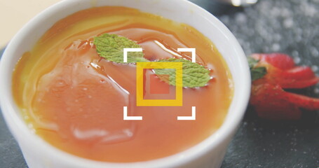 Displaying white ramekin holding orange custard topped with mint on slate board, with strawberries