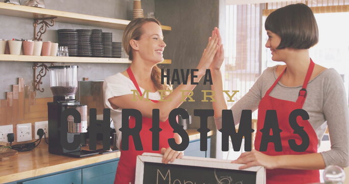 High-fiving two baristas in red aprons behind coffee counter, espresso machine and chalkboard sign - Powered by Adobe