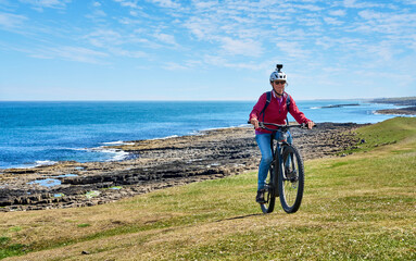 nice senior woman cycling with her electric mountain bike at the north sea coast of Northumberland , England, UK