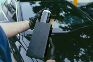 A person wearing black gloves holds a sleek black product bottle, partially enclosed in its...