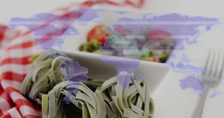 Spinach tagliatelle nests sitting on red-white checkered cloth in kitchen, with salad bowl and fork