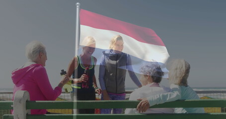 Gathering five women in sportswear on seaside walkway by bench, with water bottles and flag
