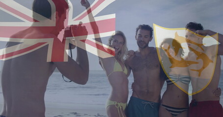 Posing four friends wearing swimwear and sunglasses at sandy beach edge, with DSLR camera