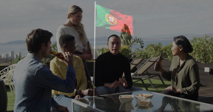 Socializing five friends sitting around coffee table with beers on rooftop terrace, Portuguese flag