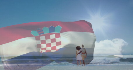 Holding hands, couple gazing at sandy beach by ocean waves with Croatian flag and sunburst effect