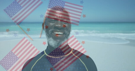 Smiling mature man in wetsuit standing on beach, with semi-transparent US flags and star overlays