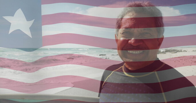 Standing older man wearing wetsuit on beach by waves, rocks, American flag overlay, copy space - Powered by Adobe
