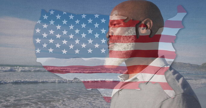 African American man in gray polo facing waves at beach, with translucent US silhouette, copy space