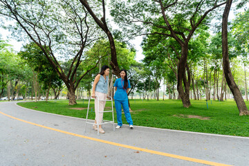 Asian nurse assists elderly woman who walks with a cane. Assists and cares for elderly female patient who is doing physical therapy in a park.