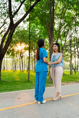 Asian female doctor takes care of elderly female patient in the park, helps the patient walk and exercises her legs and knees in the park.