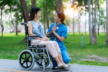 Caregiver takes elderly in wheelchair to walk in the park for health therapy, insurance concept for the elderly, happy retirement