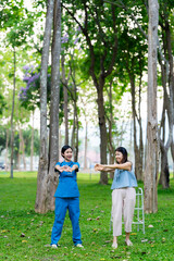Asian female doctor takes care of elderly female patient in the park, helps the patient walk and exercises her legs and knees in the park.