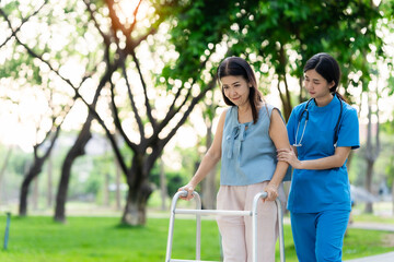 Asian nurse assists elderly woman who walks with a cane. Assists and cares for elderly female patient who is doing physical therapy in a park.