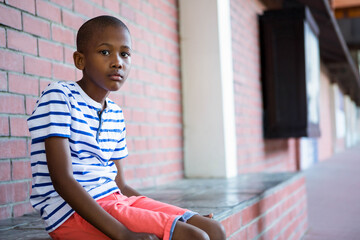 African American child sitting on stone ledge in red brick corridor with shutters, copy space