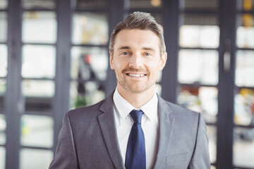 Business professional standing in modern office wearing gray suit and navy tie with glass panels
