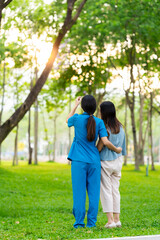 Asian female doctor takes care of elderly female patient in the park, helps the patient walk and exercises her legs and knees in the park.