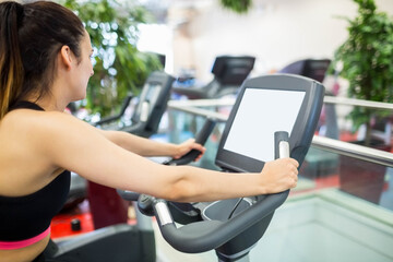 Gym patron is using elliptical machine near glass railing with digital display and cardio machines