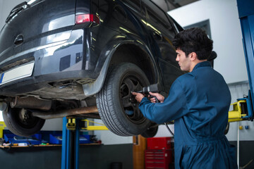 Dark hatchback rising on hydraulic lift in repair workshop showing pneumatic impact wrench on wheel