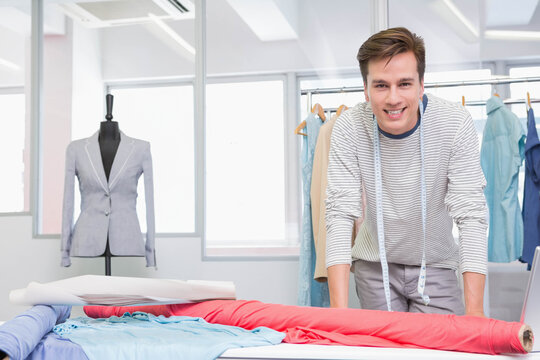 Male fashion designer using measuring tape on fabric rolls in fashion studio with mannequin