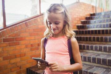Student standing on brick landing checking smartphone and wearing backpack near window