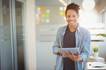 African American man wearing plaid shirt in office holding tablet near sticky notes, copy space