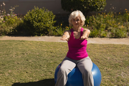 Fototapeta Senior woman balancing on blue stability ball on backyard lawn, extending arms forward at shoulders