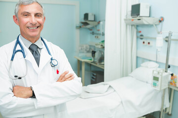 Senior male doctor standing with lab coat and stethoscope in hospital room, copy space