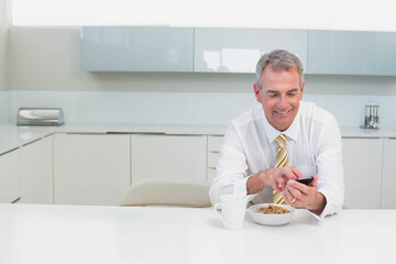 Senior man in business attire holding smartphone while eating cereal at modern kitchen, copy space