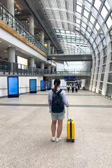 Rear view young girl in casual summer clothes with yellow suitcase and black backpack at Hong Kong...