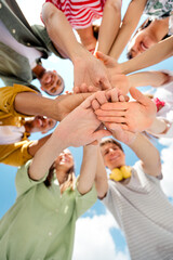 Group of young friends uniting hands outdoors on a sunny day symbolizing friendship, teamwork, and...
