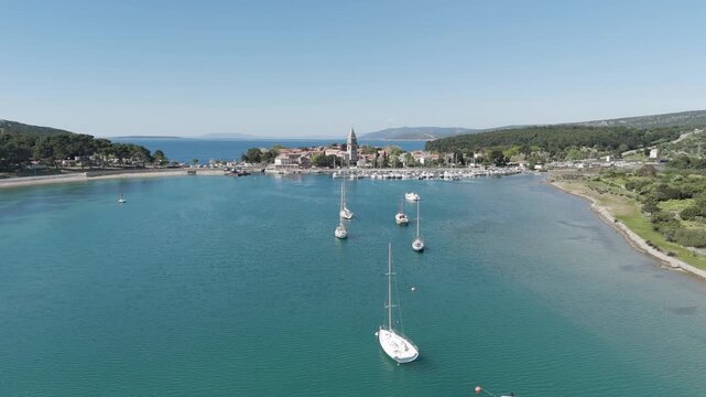 Aerial videoclip capturing sailboats passing in front of Osor Strait, showcasing scenic maritime navigation, sailing activity, and the beautiful coastal landscape from a bird's-eye perspective.