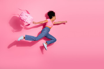Cheerful girl in pink t-shirt and blue jeans leaping joyfully against a vibrant pink background...
