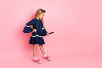 Portrait of a happy young girl in a stylish blue dress holding a smartphone against a vibrant pink...