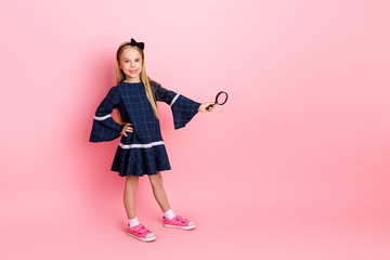 Charming girl with a magnifying glass posing against a pink background dressed stylishly in a blue...