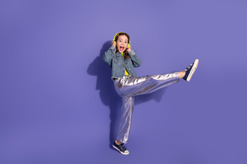 Excited young girl in trendy silver pants and denim jacket posing playfully against a vibrant...