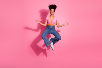 Young cheerful woman meditating in midair against pink background wearing casual stylish outfit...