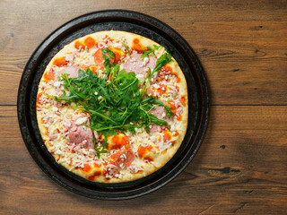 A pizza with ham and spinach on a black tray. The pizza is sitting on a wooden table. Fine Italian...