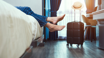 satisfied joyful solo traveler woman taking off footwear, lying on a bed in hotel bedroom after check-in with suitcase in the room, having rest after long trip. enjoy summer holiday and vacation.