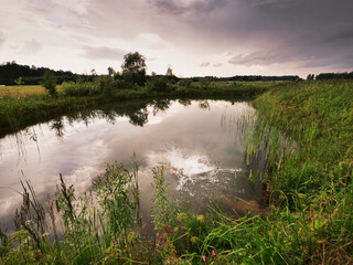 A man is jumping into a pond wearing an orange swimsuit at dusk. The sky is cloudy and the water is...
